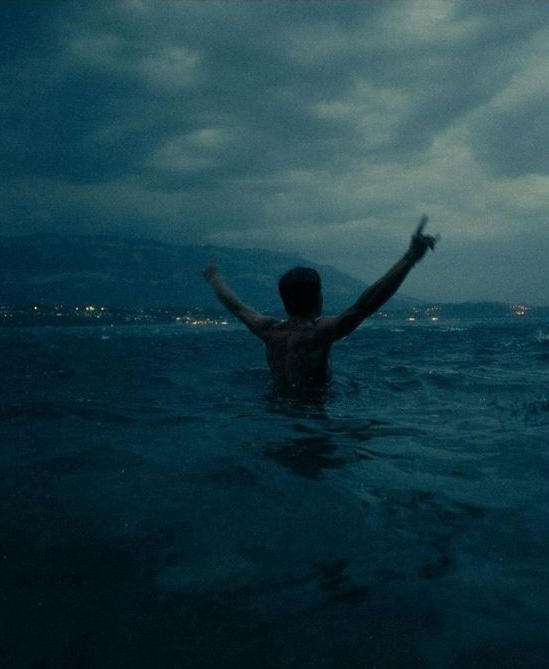 Figure raising arms in the sea at dusk